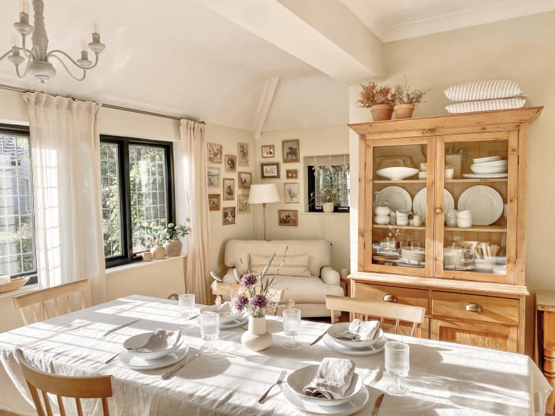 beige dining room with large wood table with pale tablecloth, large wood hutch, cozy corner chair, and gray chandelier