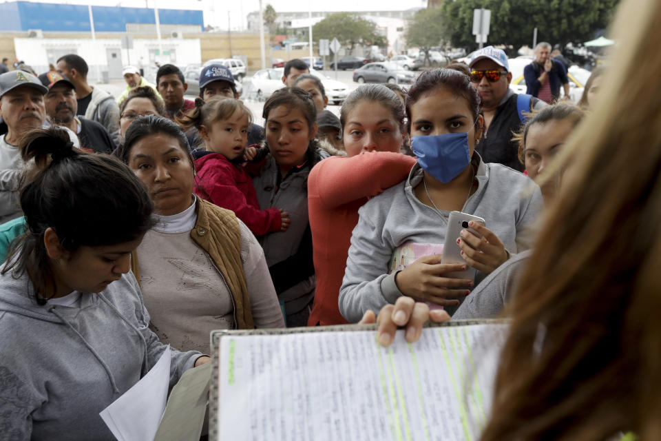 FILE - In this Oct. 23, 2018 file photo, women look on as numbers and names are called to cross the border and request asylum in the United States, in Tijuana, Mexico. The Mexican government said Friday, Jan. 25, 2019 that the United States plans to return 20 migrants per day to Mexico as they await an answer to their U.S. asylum claims. The spokesman for Mexico's Foreign Relations Department says Mexico doesn't agree with the move, but will accept the migrants at the San Ysidro border crossing, near Tijuana. (AP Photo/Gregory Bull, File)