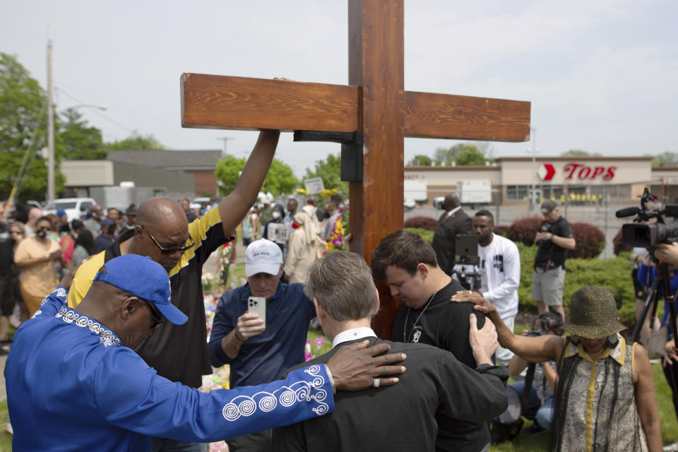 FILE - A group prays next to a cross at the site of a memorial for the victims of the Buffalo supermarket shooting outside the Tops Friendly Market on Saturday, May 21, 2022, in Buffalo, N.Y. (AP Photo/Joshua Bessex, File)