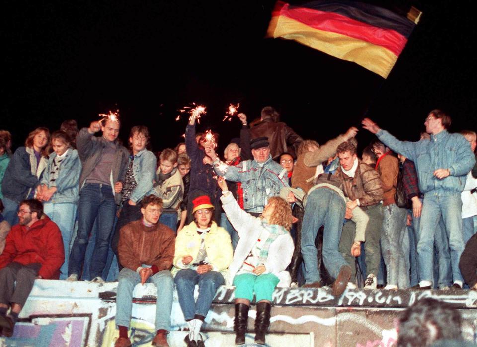 ARCHIV - 10.11.1989, Berlin: Mit Wunderkerzen in den Händen freuen sich die Menschen auf der Berliner Mauer über die Öffnung der deutsch-deutschen Grenzen.  Die Bilder vom Mauerfall wirkten, was die Mode angeht, lange komisch. Heute hat sich das geändert. Die 80er Jahre sind schwer im Trend. (Bild: DB/dpa)