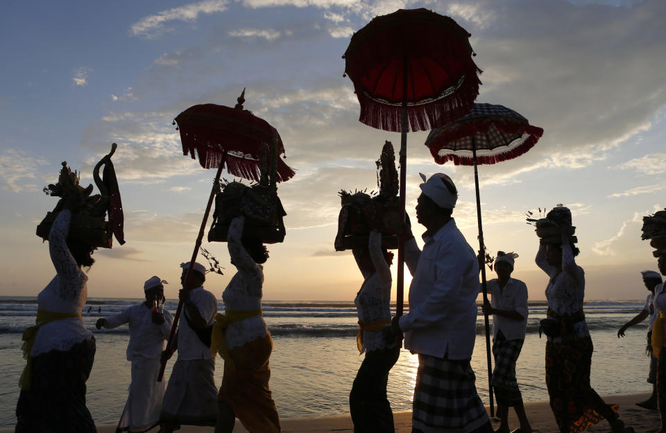 In this April 19, 2019, file photo, Balinese Hindus walk on a beach carrying sacred ornaments during a full moon Hindu ritual in Bali, Indonesia. (AP Photo/Firdia Lisnawati, File)