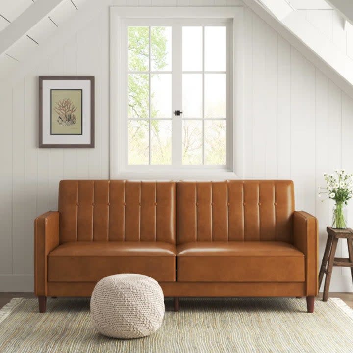 rectangular faux leather brown couch in open space with small pouf
