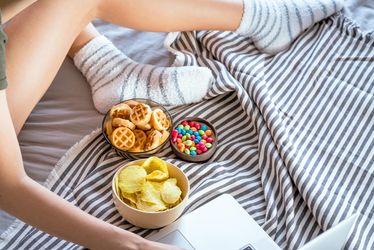 Person on bed with three bowls of snacks next to laptop.