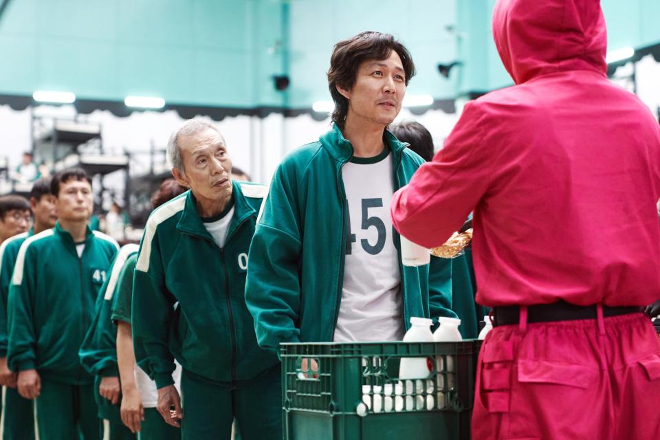 "Squid Game" scene showing several contestants in numbered green tracksuits, including Player 456 (Lee Jung-jae) and Player 001 (Oh Yeong-su). Guards in pink uniforms