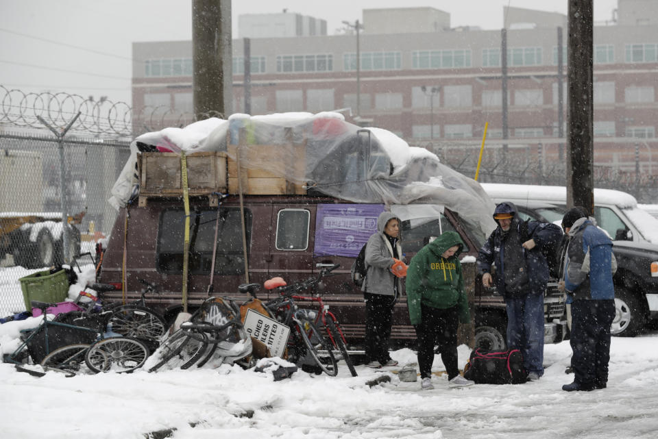 A group of people who share living space in a van, left, gather on a street in Seattle's SODO neighborhood, Monday, Feb. 11, 2019, in Seattle. Thomas Bolander, right, said that finding different ways to keep warm and dry out was the hardest part of being unsheltered during the winter weather that has dumped snow across the Northwest. Seattle's metro area has already been hit by three snowstorms in February, making it the snowiest month in Seattle in more than 30 years. (AP Photo/Ted S. Warren)