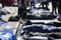 People sit next to the bodies of earthquake victims outside a hospital in Antakya, southeastern Turkey, Thursday, Feb. 9, 2023. Thousands who lost their homes in a catastrophic earthquake huddled around campfires and clamored for food and water in the bitter cold, three days after the temblor and series of aftershocks hit Turkey and Syria. (AP Photo/Khalil Hamra)