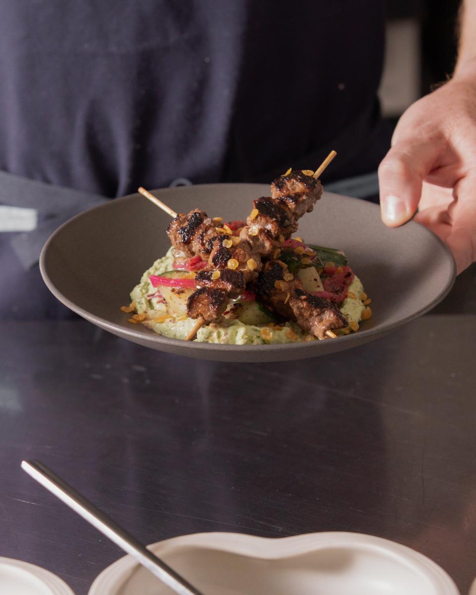 The Kangaroo Tucker at Isla & Co. features Australian rubbed Kangaroo skewered and grilled over herbed tahini, marinated cucumbers, pickled onions and fried lentils.