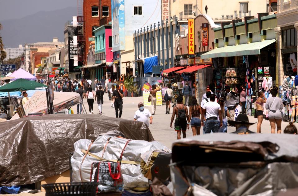 Tarps cover rows of belongings next to people walking along shops and restaurants in Venice