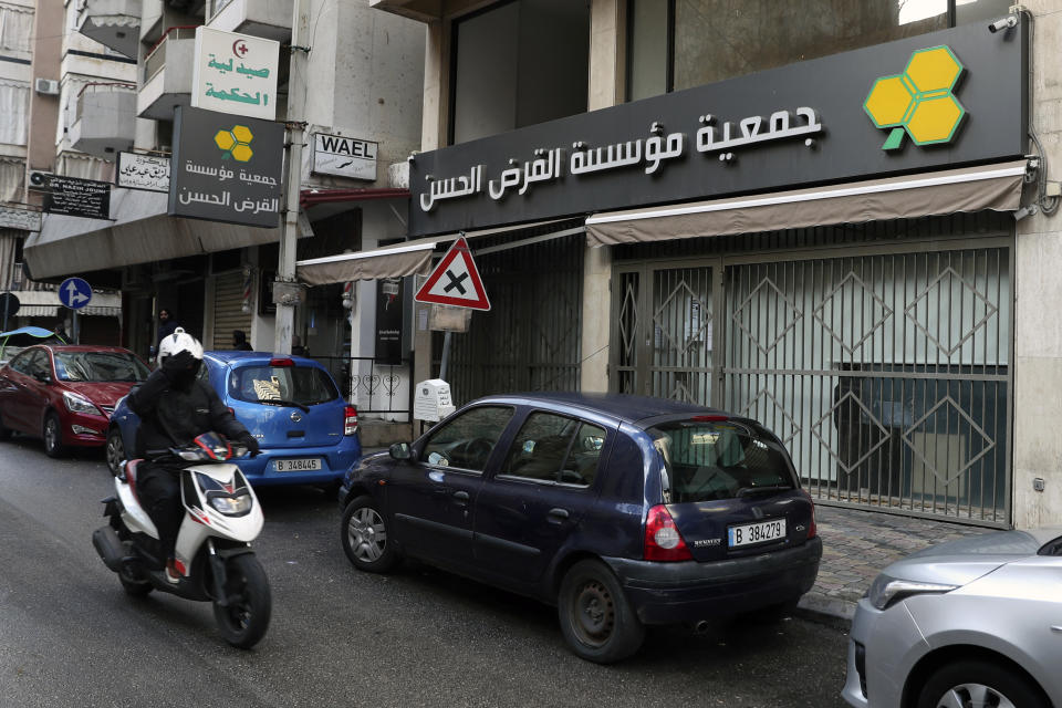 A man on a scooter passes a branch of the Hezbollah-run Qard al-Hassan Association, in Beirut, Lebanon, Wednesday, Jan. 20, 2021. As more Lebanese fall into poverty in the country's economic crisis, increasing numbers are turning to the financial arm of the Iranian-backed Hezbollah militant group for help. Qard al-Hassan provides small, interest-free loans in dollars at a time when Lebanese are desperate for hard currency and commercial banks are not lending. Those seeking a loan must put up gold as collateral or bring in a guarantor and can receive a loan of up to $5,000. (AP Photo/Bilal Hussein)