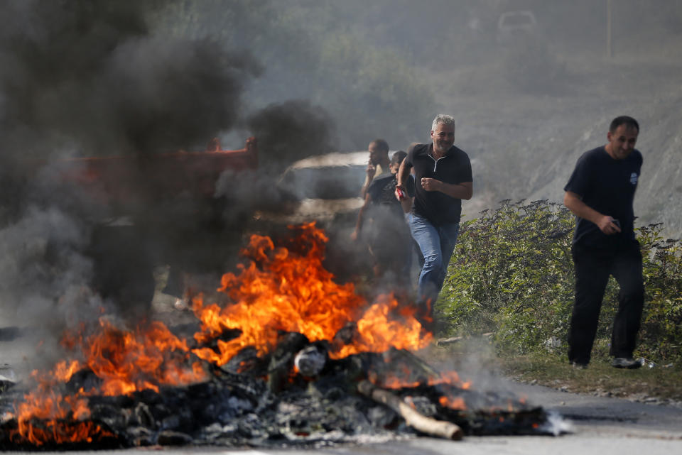 Kosovo Albanians run past a fire burning at a roadblock in Vojtesh, Kosovo, Sunday, Sept. 9, 2018. Kosovo Albanians burned tires and blocked roads with wooden logs, trucks and heavy machinery on a planned route by Serbia's President Aleksandar Vucic who was trying to reach the village of Banje while visiting Serbs in the former Serbian province. (AP Photo/Visar Kryeziu)