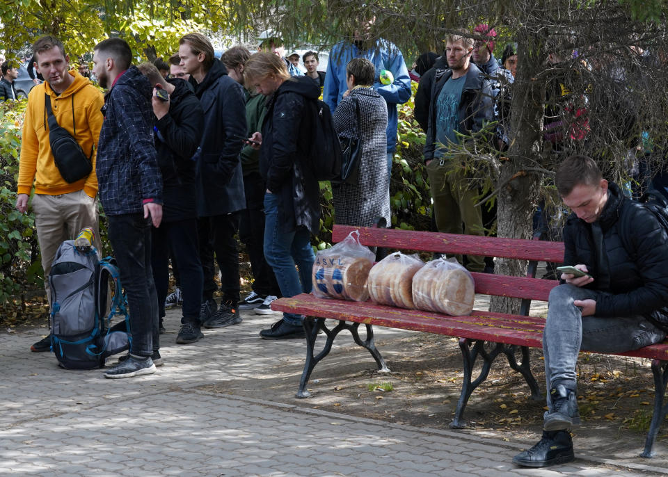 A man sits on a bench checking his phone as Russian citizens line up outside a public service center in Kazakhstan.