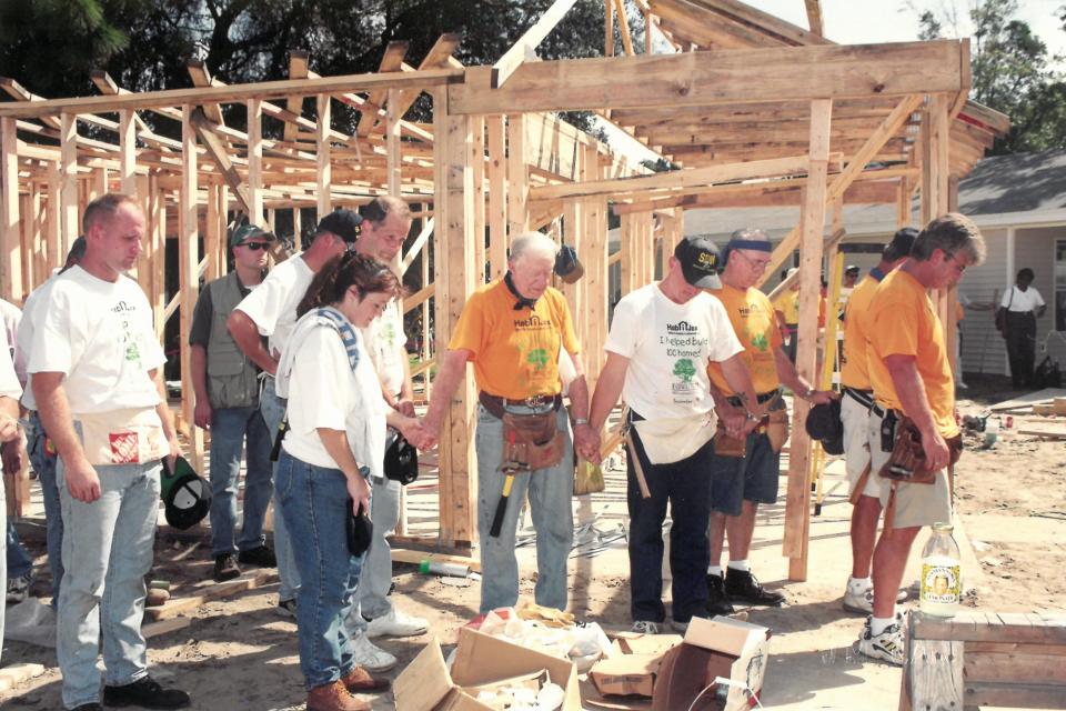 In 2000, former President Jimmy Carter (center) leads a prayer at a Habitat for Humanity blitz build as part of the Carter Work Project.