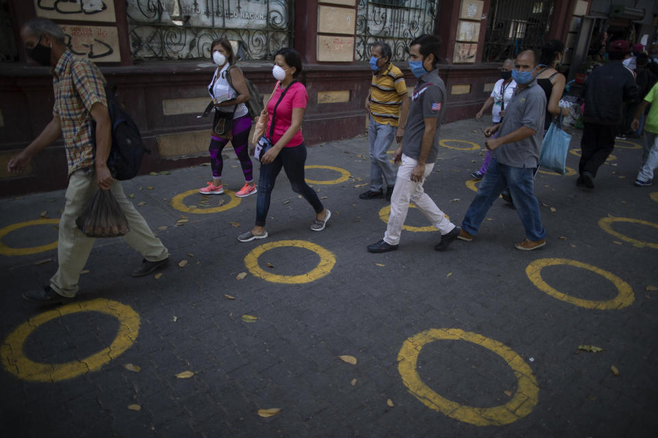 Yellow circles on a pavement serve as visual cues to help shoppers adhere to social distancing when lines form, to curb the spread of the new coronavirus, near a popular market in Caracas, Venezuela, Saturday, May 23, 2020. Evidence is mounting that these type of markets contributed to the spread of coronavirus in Latin America. (AP Photo/Ariana Cubillos)