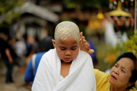 A woman smears a boy with paste made from thanaka bark after his hair was shaved in preparation for an annual Poy Sang Long celebration, a traditional rite of passage for boys to be initiated as Buddhist novices, in Mae Hong Son, Thailand, April 2, 2018. REUTERS/Jorge Silva