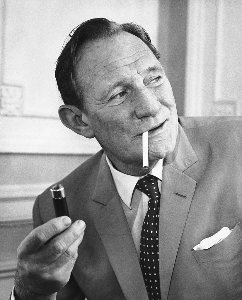 A man in a suit and polka dot tie holding a lighter and smoking a cigarette