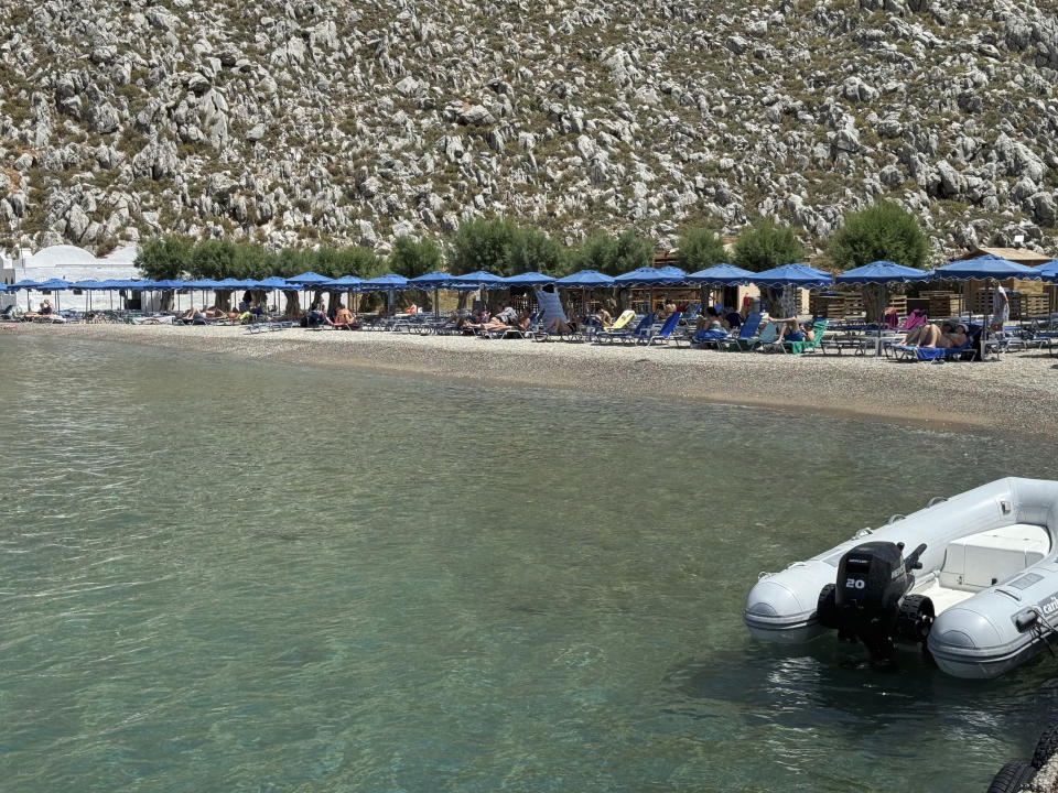 People sit on the beach of Agios Nikolaos from where British doctor and television presenter Michael Mosley, is believed to have set out, on the southeastern Aegean Sea island of Symi, Greece, Friday, June 7, 2024. Greek police say an ongoing major search and rescue operation on the small eastern Aegean island of Symi has still not located British doctor and television presenter Michael Mosley, who went missing on Wednesday afternoon after reportedly going for a walk. (AP Photo/Antonis Mystiloglou)