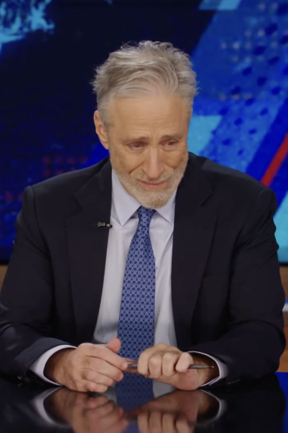 Jon Stewart sitting behind a desk on the set of 