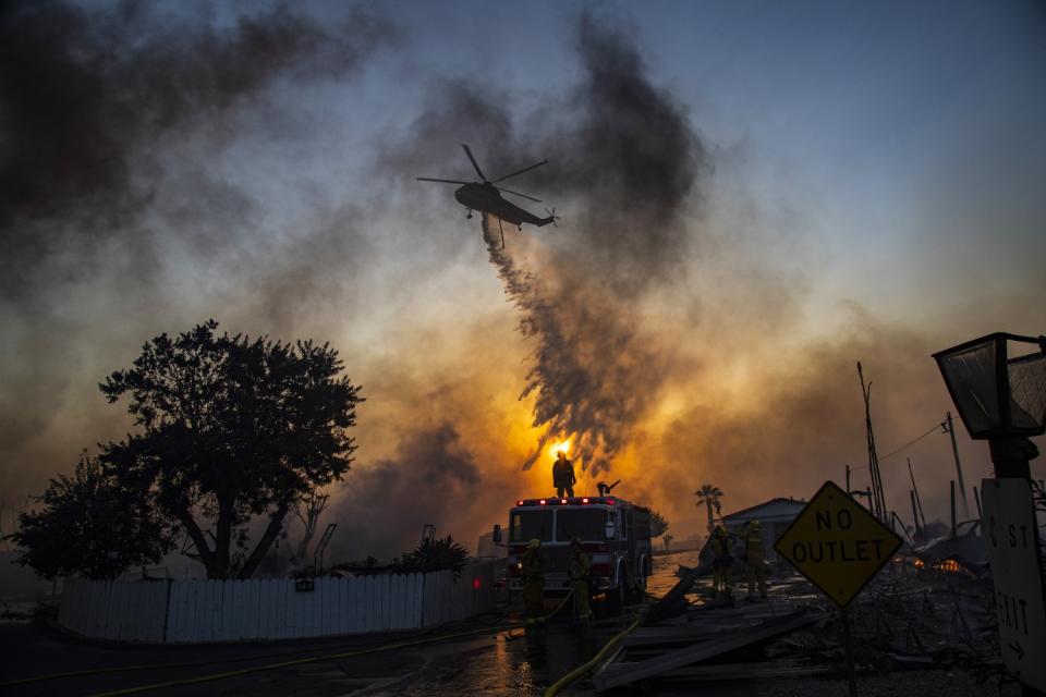 A helicopter drops water on burning mobile homes.