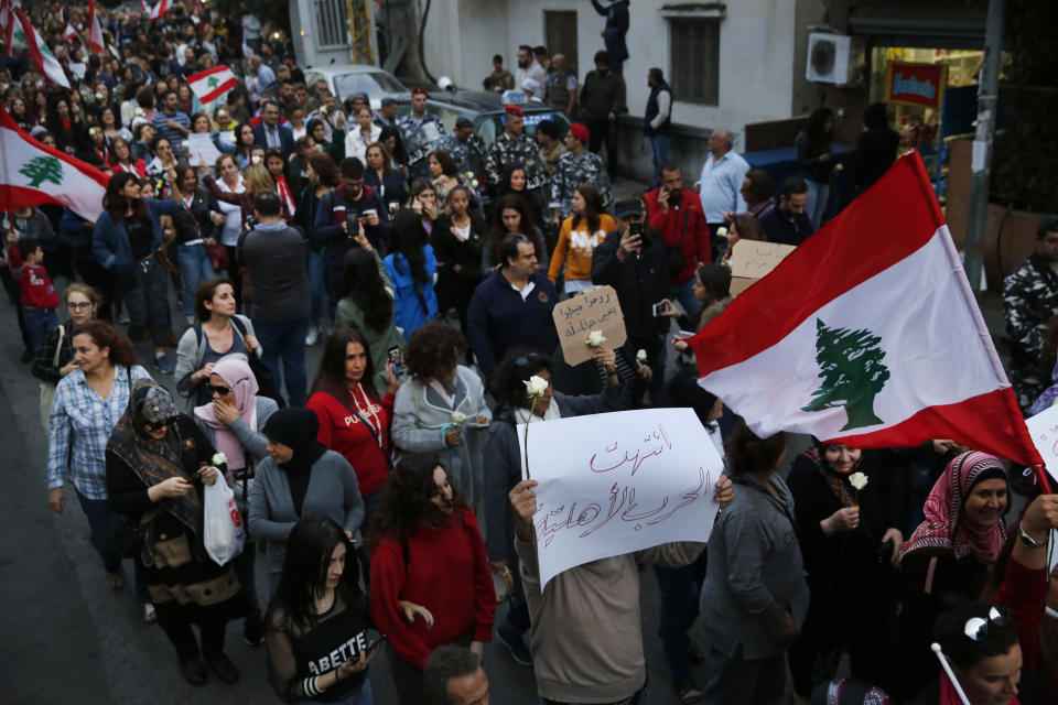 Lebanese women march during a protest at a former Beirut frontline between Christian district of Ain el-Rummaneh and a Muslim Shiite district of Shiyah, in Beirut, Lebanon, Wednesday, Nov. 27, 2019. Hundreds of Lebanese women marched across a former front line in the Lebanese capital carrying white roses and Lebanese flags to denounce overnight clashes between rival groups that injured dozens of people. The Arabic placard front reads:"The civil war is over." (AP Photo/Hussein Malla)