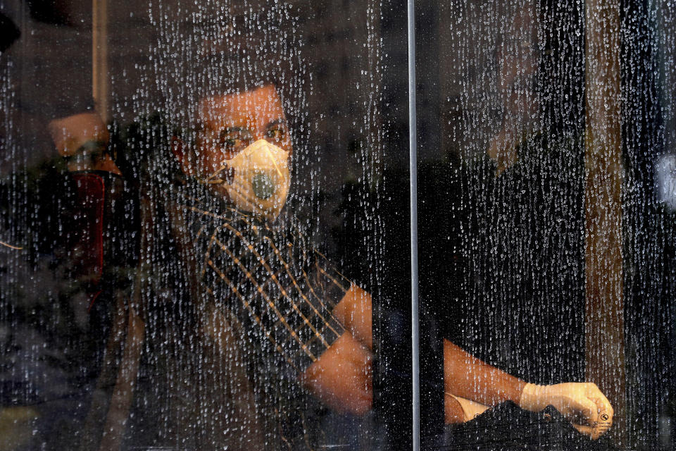 A commuter looks through a water-stained window wearing a mask and gloves to help guard against the Coronavirus, on a public bus in downtown Tehran, Iran, Sunday, Feb. 23, 2020. Iran's health ministry raised Sunday the death toll from the new virus to 8 people in the country, amid concerns that clusters there, as well as in Italy and South Korea, could signal a serious new stage in its global spread. (AP Photo/Ebrahim Noroozi)