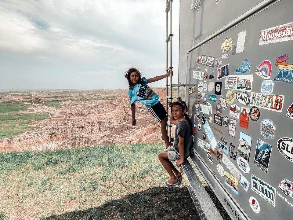 Kids posing on side of large gray RV home with bumper stickers