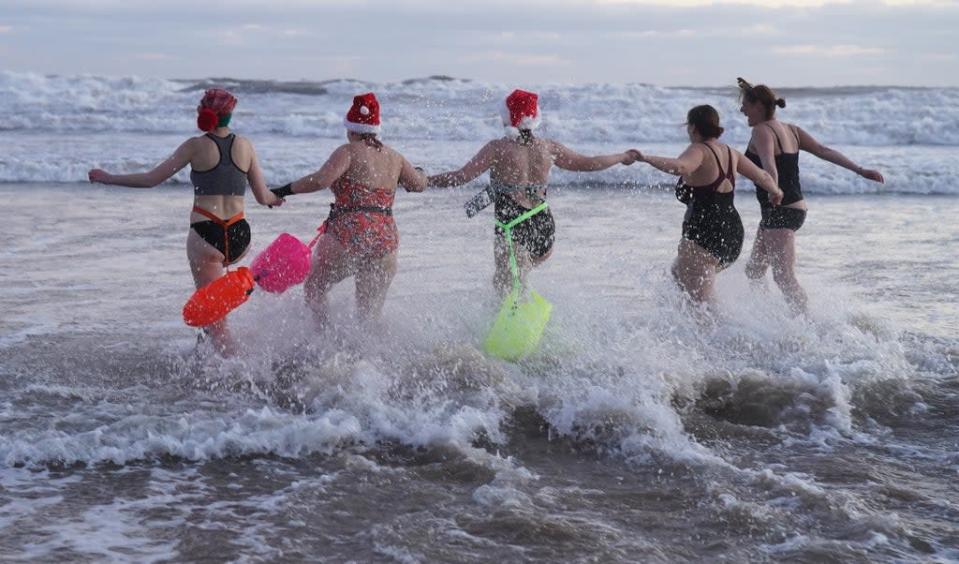 A group of swimmers run into the water for a Christmas Day dip at Tynemouth Beach (Owen Humphreys/PA) (PA Wire)