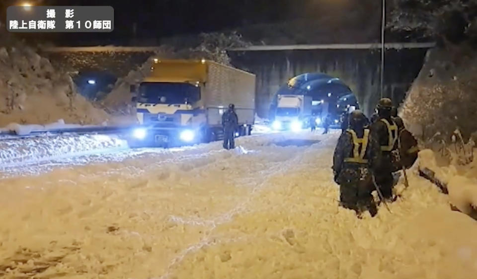 In this image made from video provided by the Japan Ground Self-Defense Force, its members watch vehicles to move foreword after they clear snow off to make enough space for vehicles to move on an expressway near or in Sekigahara, central Japan, Wednesday, Jan. 24. 2024, following heavy snow in the area. Weather officials in Japan predicted more heavy snow Thursday, a day after nearly 800 vehicles were trapped for hours on an expressway in central Japan. (Japan Ground Self-Defense Force via AP)