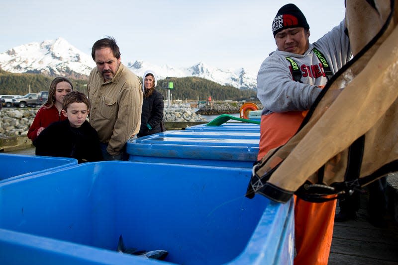 Locals watch as workers unload fish into crates on a public dock in Cordova, Alaska.