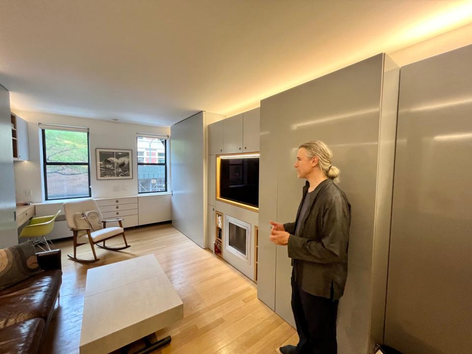 Robert Garneau stands in the apartment against a smooth, gray wall. 