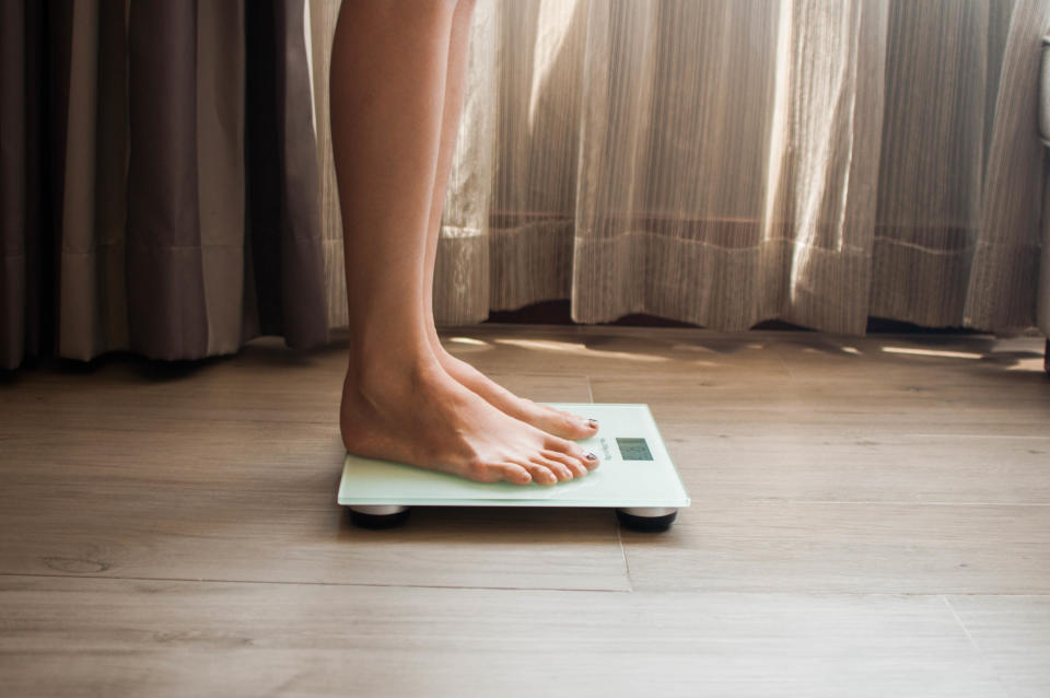 A low-angle view of a young woman who is weighing herself in a weighing scale