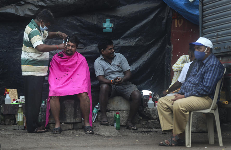 A roadside barber wearing mask as a precaution against the coronavirus gives hair cut to a man as others wait for their turn in Mumbai, India, Sunday, Jan. 3, 2021. India authorized two COVID-19 vaccines on Sunday, paving the way for a huge inoculation program to stem the coronavirus pandemic in the world’s second most populous country. (AP Photo/Rafiq Maqbool)