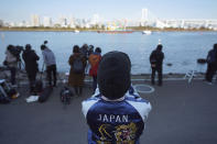 A woman watches at the Olympic Symbol being transported on a barge in the Odaiba section Tuesday, Dec. 1, 2020, in Tokyo. The five Olympic rings are back in Tokyo Bay. They were removed for maintenance four months ago shortly after the Tokyo Olympics were postponed until next year because of the COVID-19 pandemic. (AP Photo/Eugene Hoshiko)