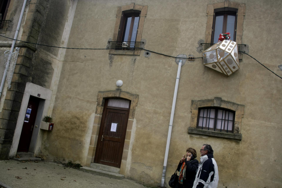 People walk past a model meant to represent a UFO hanging outside a window in the town of Bugarach, France, Thursday, Dec. 20, 2012. The clock is ticking down to Dec. 21, the supposed end of the Mayan calendar, and from China to California to Mexico, thousands are getting ready for what they think is going to be a fateful day. The sleepy town of Bugarach, nestled in the French Pyrenees mountains, is bracing for the arrival of hundreds of New Age enthusiasts and UFO believers that want to witness the end of the Mayan Long Count calendar. (AP Photo/Marko Drobnjakovic)