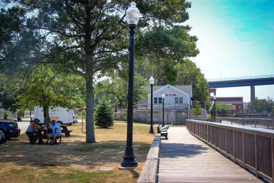 Visitors to Fall River's waterfront sit in the shade by the boardwalk near the boating center, on July 24, 2022.