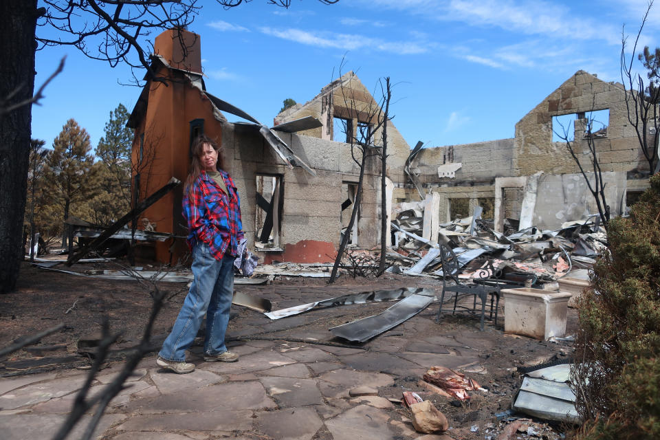 Jeanne Welnick stands amid the ruins of her home on the outskirts of Flagstaff, Ariz., Thursday, April 28, 2022. A massive wildfire that started Easter Sunday burned about 30 square miles and more than a dozen homes, hopscotching across the parched landscape. (AP Photo/Felicia Fonseca)