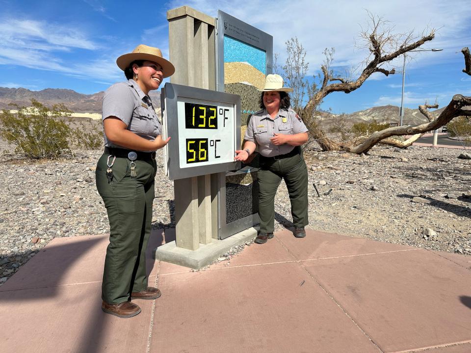 Two park rangers posing next to a temperature display that reads "132 degrees Fahrenheit"