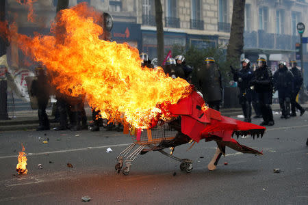 Flames from a burning cardboard dragon in a caddy are seen near French CRS riot police during clashes as part of the traditional May Day labour union march in Paris, France, May 1, 2017. REUTERS/Gonzalo Fuentes