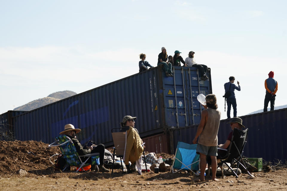 Activists gather near and sit on newly installed shipping containers along the border creating a wall between the United States and Mexico in San Rafael Valley, Ariz., Thursday, Dec. 8, 2022. Work crews are steadily erecting hundreds of double-stacked shipping containers along the rugged east end of Arizona’s boundary with Mexico as Republican Gov. Doug Ducey makes a bold show of border enforcement even as he prepares to step aside next month for Democratic Governor-elect Katie Hobbs. (AP Photo/Ross D. Franklin)