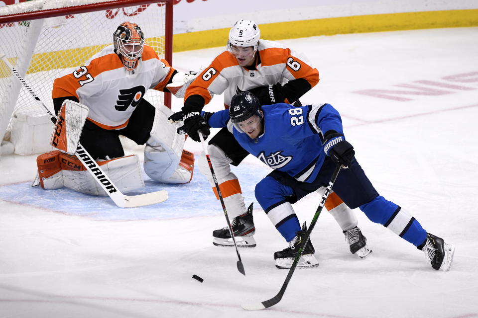 Winnipeg Jets' Jack Roslovic (28) tries to skate around Philadelphia Flyers' Travis Sanheim (6) to shoot against Flyers goaltender Brian Elliott (37) during first-period NHL hockey game action in Winnipeg, Manitoba, Sunday, Dec. 15, 2019. (Fred Greenslade/The Canadian Press via AP)