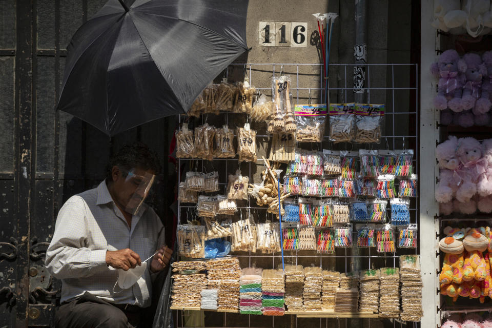 A snack vendor fixes his mouth and nose covering, which he wears due to the COVID-19 pandemic, on a sidewalk in downtown Mexico City, Friday, Oct. 30, 2020. Prior to the coronavirus pandemic, Mexico’s economy was in recession, and that only deepened with the economic shutdown provoked by measures aimed at slowing the spread of COVID-19 during the second quarter. (AP Photo/Fernando Llano)