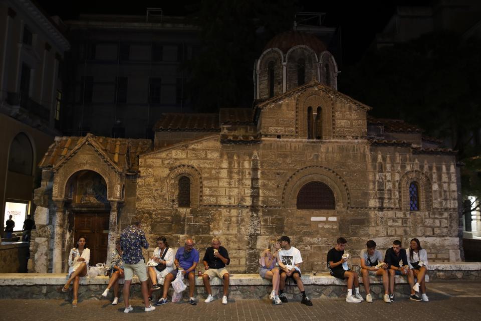 People gather in front of the Kapnikarea Orthodox church after the midnight closure of the restaurant and bars in Athens, Friday, Aug. 21, 2020. Authorities in Greece are using free on-the-spot tests for ferry passengers and nightlife curfews on popular islands to stem a resurgence of the coronavirus after the country managed to dodge the worst of the pandemic. The number of confirmed virus cases and deaths in Greece remains lower than in many other European countries. (AP Photo/Thanassis Stavrakis)