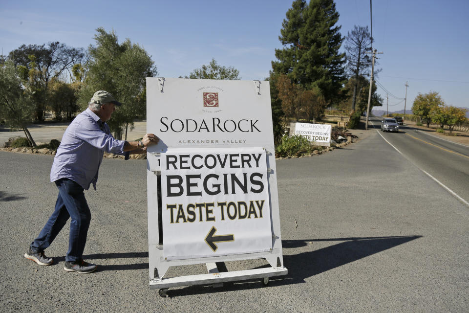 In this Wednesday, Nov. 6, 2019 photo, owner Ken Wilson rolls out a sign for passing motorists after opening a tasting area at his wildfire incinerated Soda Rock Winery in Healdsburg, Calif. If you're worried that wildfires might have created shortages of Northern California's 2019 Cabernet Sauvignon, or even just imparted it with an undesirable smoky flavor, you can relax. The wine is just fine. For now. (AP Photo/Eric Risberg)