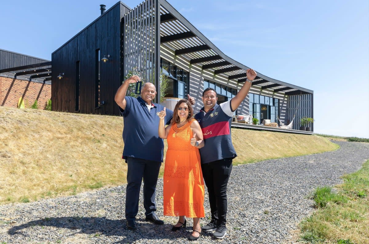 Uttam Parmar, 58, with his wife Raki and son Aaron, celebrating in front of the £3,000,000 property he has won in Cornwall (Omaze/PA) (PA Media)