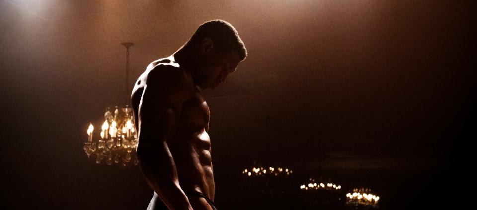 Jonathan Majors standing shirtless in a dimly lit room with chandeliers above him in "Magazine Dreams."