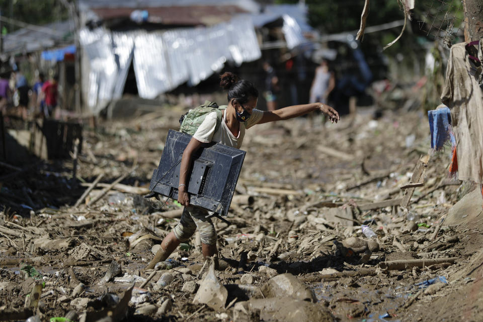 A woman carries a computer monitor she retrieved from her house at the typhoon-damaged Kasiglahan village in Rodriguez, Rizal province, Philippines, Friday, Nov. 13, 2020. Thick mud and debris coated many villages around the Philippine capital Friday after Typhoon Vamco caused extensive flooding that sent residents fleeing to their roofs and killing dozens of people. (AP Photo/Aaron Favila)