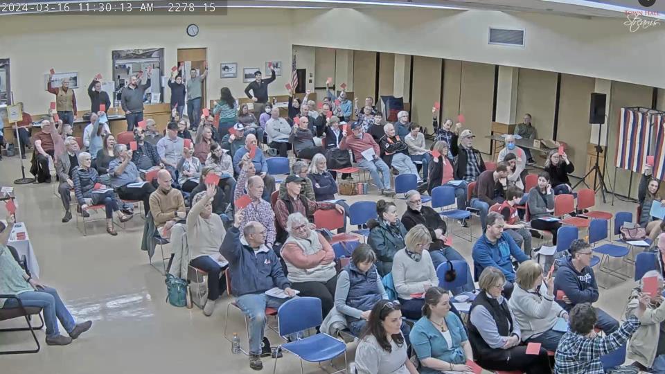 Newington town residents raise their cards at the Town Meeting on March 16, 2024, to allow Greenland resident Douglas Wilson to speak. He spoke in favor of Article 15, which would ban voting machines from Newington. However, the measure was ultimately defeated 85-11.