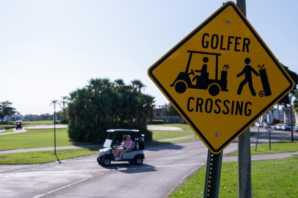 David Margalit, center, Delray Beach, and Klemant Mayzel, Boynton Beach, drive a golf cart across a street under a u0022Golfer Crosseru0022 sign at King's Point Golf and Country Club in Delray Beach.