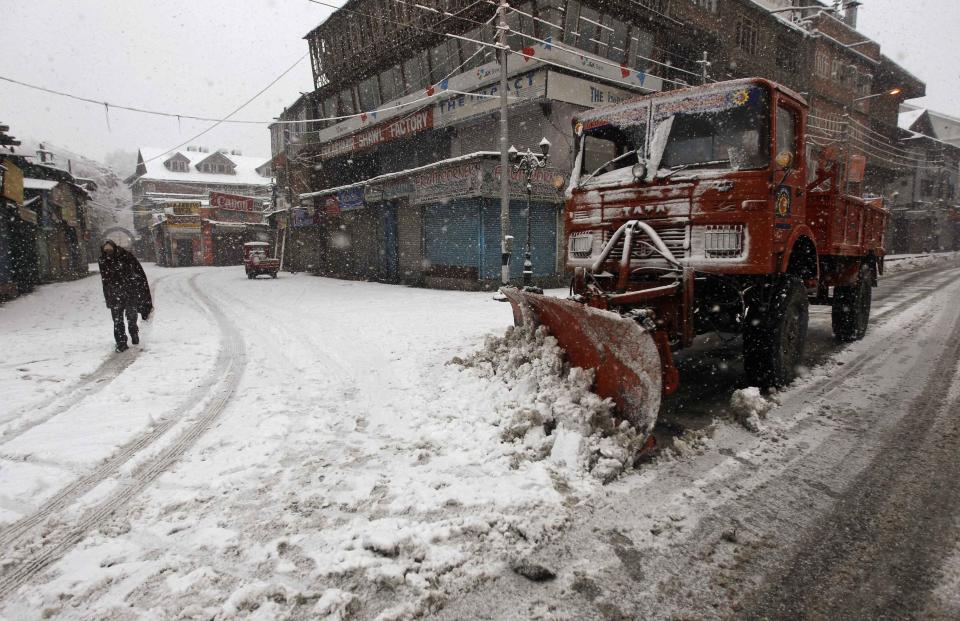 A snow-clearing machine removes snow from a road during snowfall on a cold winter morning in Srinagar