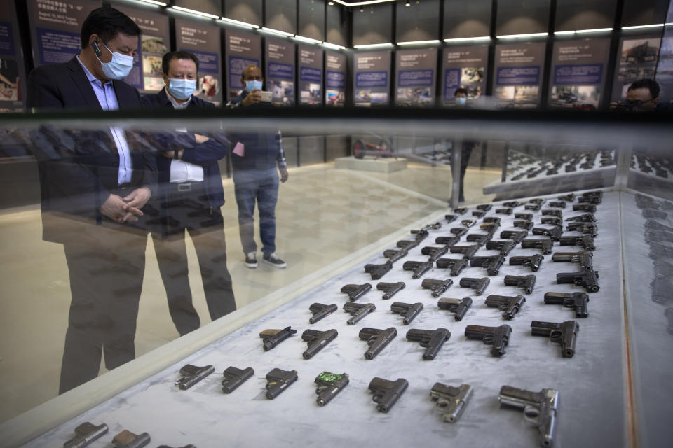 Chinese government officials look at a display of handguns seized in security operations in Xinjiang at the Exhibition of the Fight Against Terrorism and Extremism in Urumqi in northwestern China's Xinjiang Uyghur Autonomous Region, as seen during a government organized visit, on April 21, 2021. Four years after Beijing's brutal crackdown on largely Muslim minorities native to Xinjiang, Chinese authorities are dialing back the region's high-tech police state and stepping up tourism. But even as a sense of normality returns, fear remains, hidden but pervasive. (AP Photo/Mark Schiefelbein)