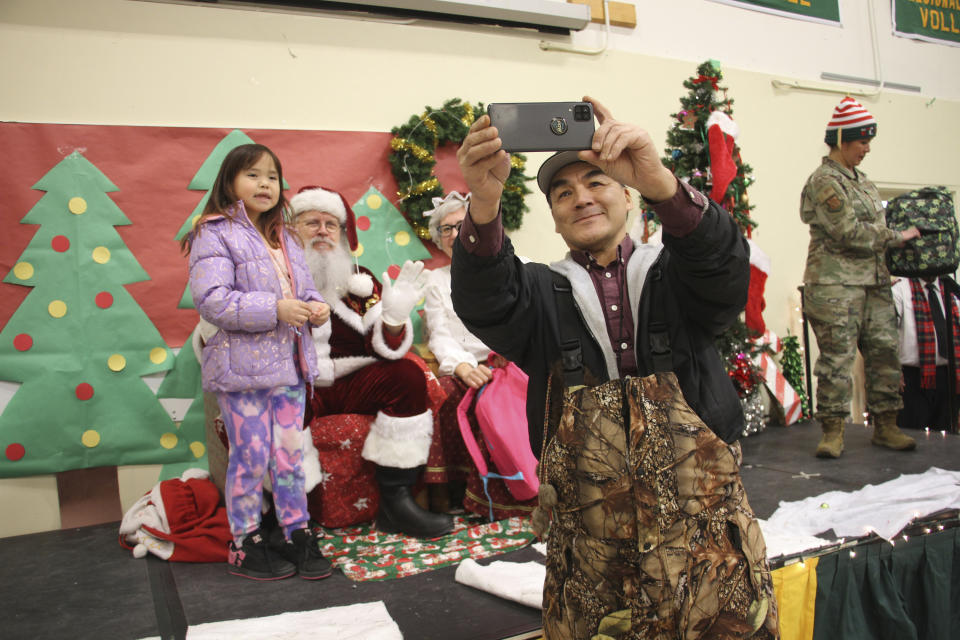 A parent takes a selfie with a child and Santa and Mrs. Claus in Nuiqsut, Alaska, on Nov. 29, 2022. Operation Santa Claus, the Alaska National Guard's outreach program, attempts to bring Santa and Mrs. Claus and gifts to children in two or three Alaska Native villages each year, including Nuiqsut in 2022. (AP Photo/Mark Thiessen)